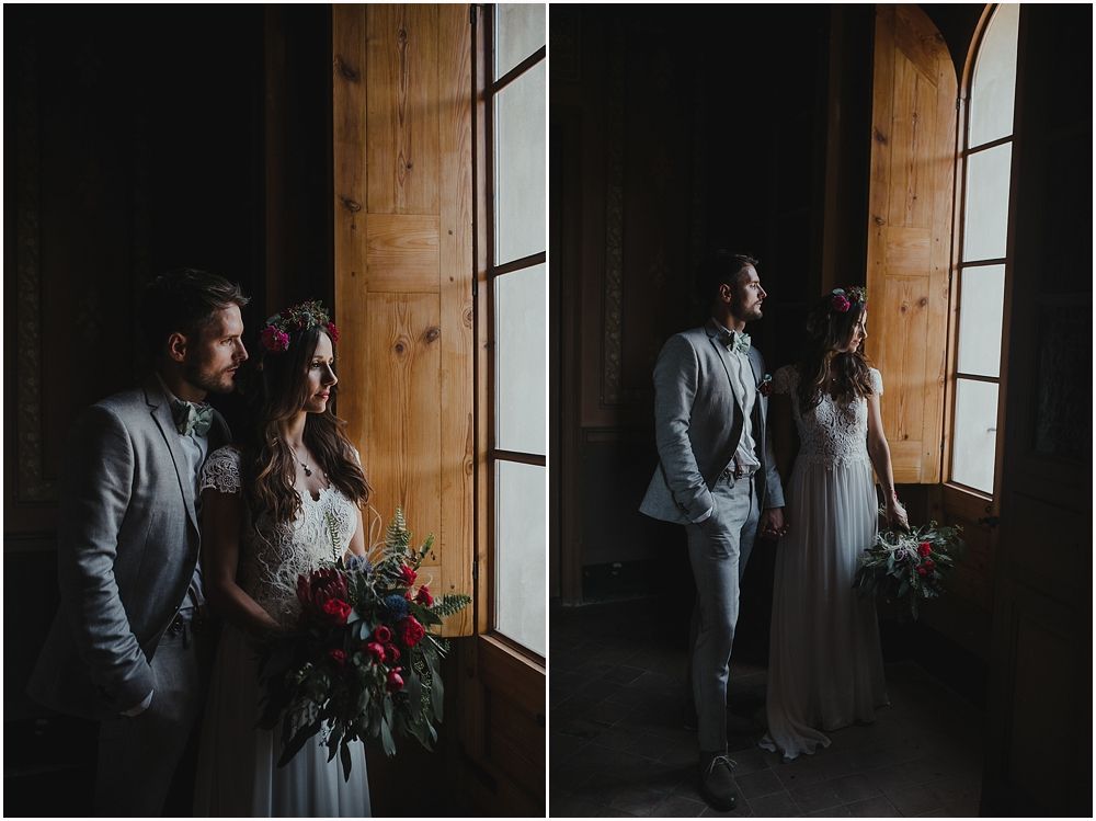 Moody wedding portraits by large window showing light and dark contrasts.