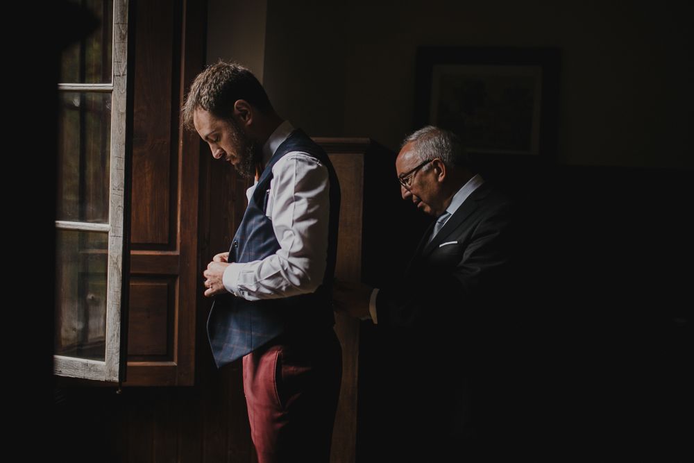 Two people in formal wear stand near a window in contrasting light and shadow.