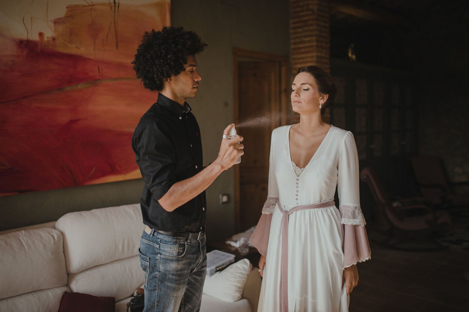 Wedding day preparations show stylist assisting with final touches in modern living room setting.