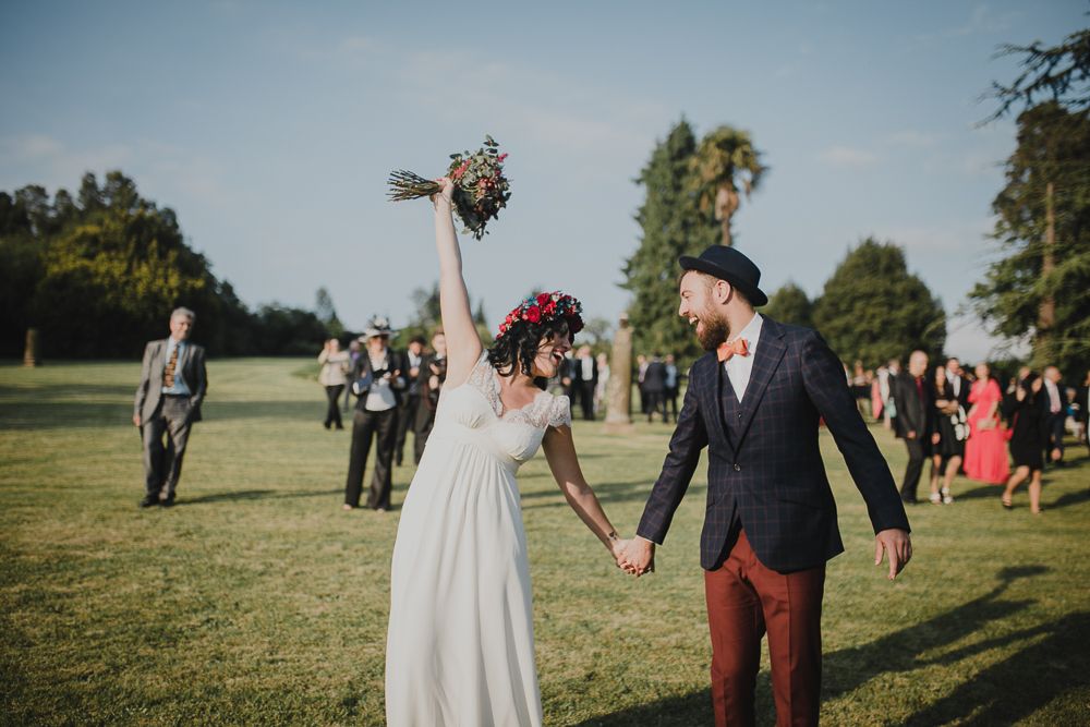 A celebratory moment on a sunny lawn with raised bouquet and burgundy accents.