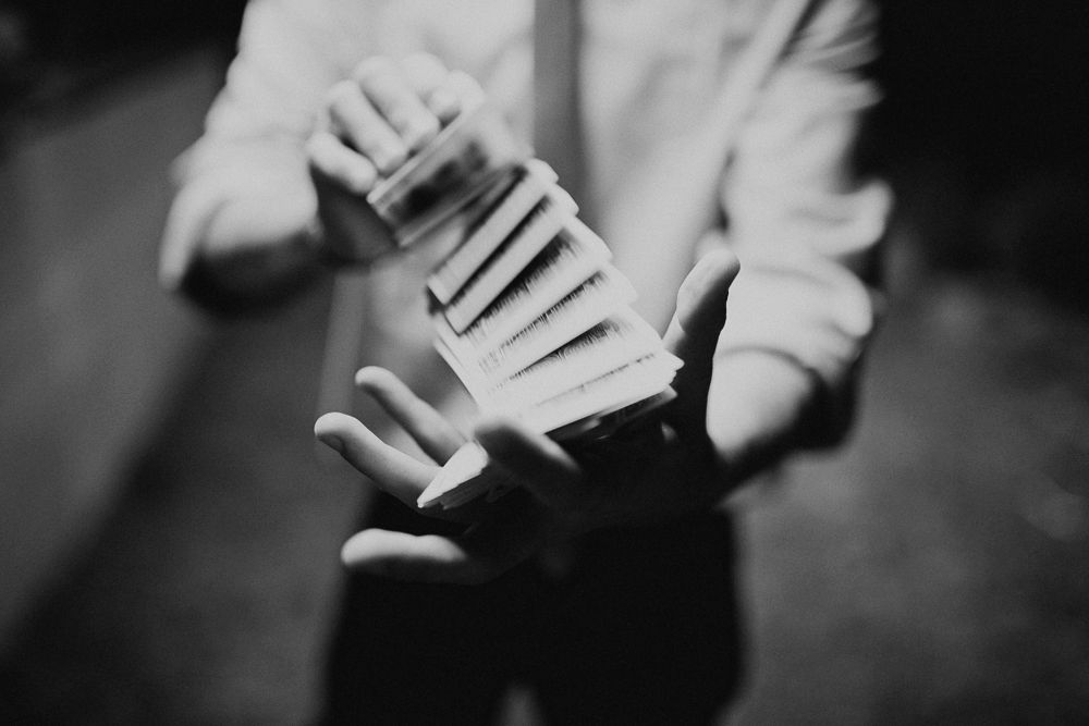Magician in white shirt performing with a playing card in dramatic lighting.