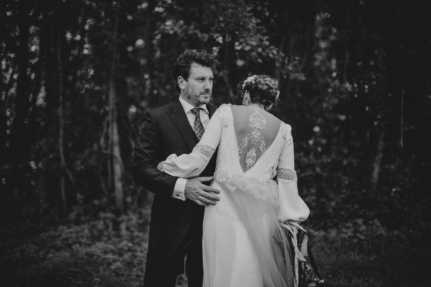 Black and white wedding portrait capturing intimate moment in forest setting.