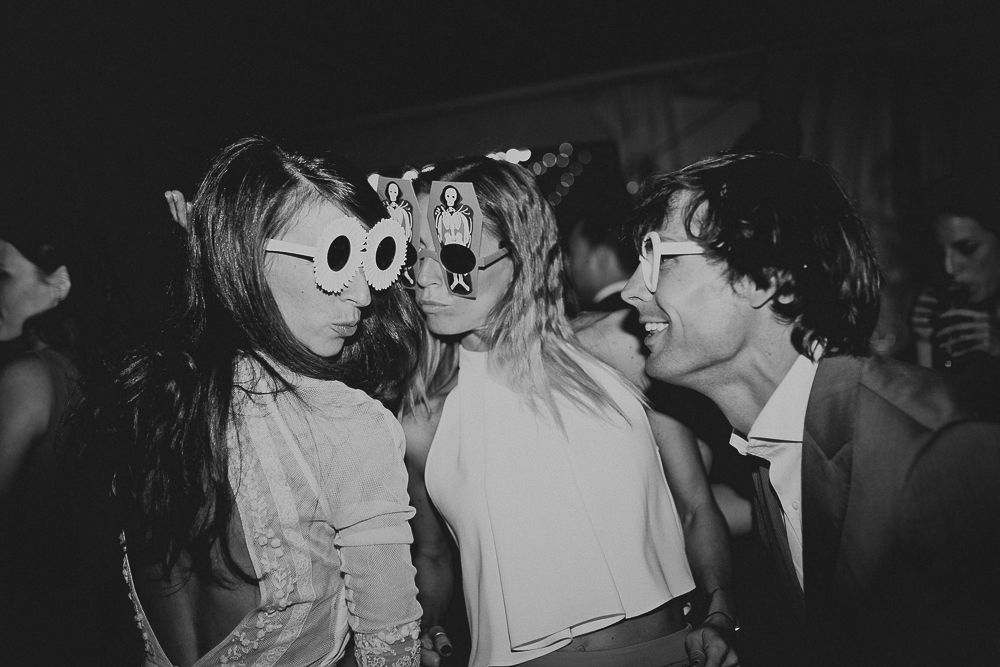 Party guests wearing fun sunglasses and formal attire at nighttime celebration.