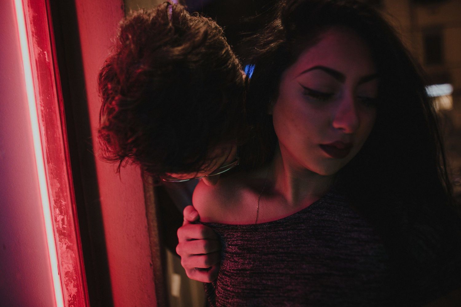 A couple embracing in the glow of red neon lights against a dark background.