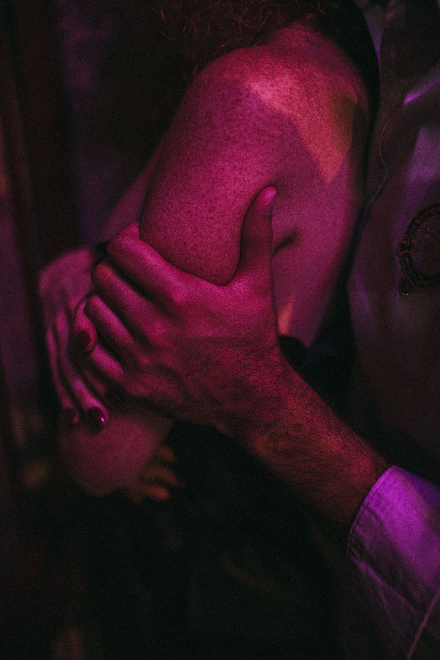 Artistic photo of hands embracing in pink and purple lighting creating a romantic atmosphere.