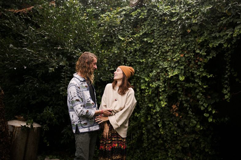 A couple shares a tender moment in front of a verdant garden wall.