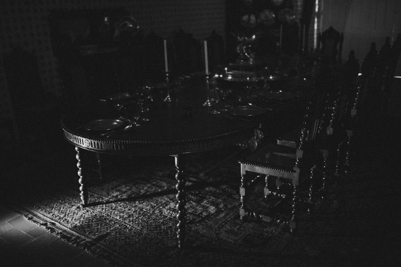 Dark atmospheric interior scene with antique wooden dining table and chairs.
