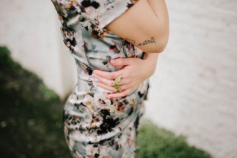 Close up of hands resting on a floral patterned dress against white background.