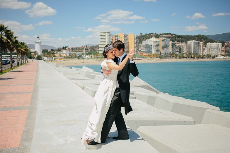 Wedding couple dancing together on seaside promenade with coastal city backdrop.
