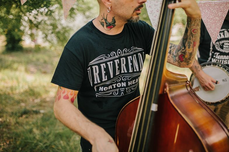 Close-up shot of a tattoo-covered bassist playing an upright bass while wearing a band t-shirt.