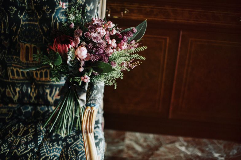 Moody wedding bouquet with deep red and purple flowers against dark wood paneling.