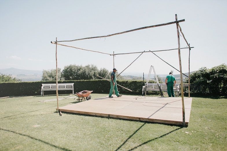 Construction frame being set up on a hilltop lawn with workers in green uniforms.