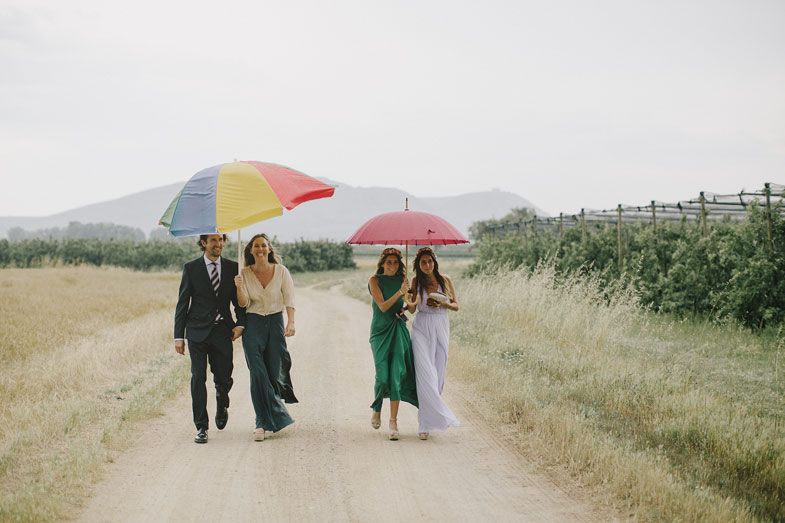 Wedding party walking along a country path with colorful umbrellas.