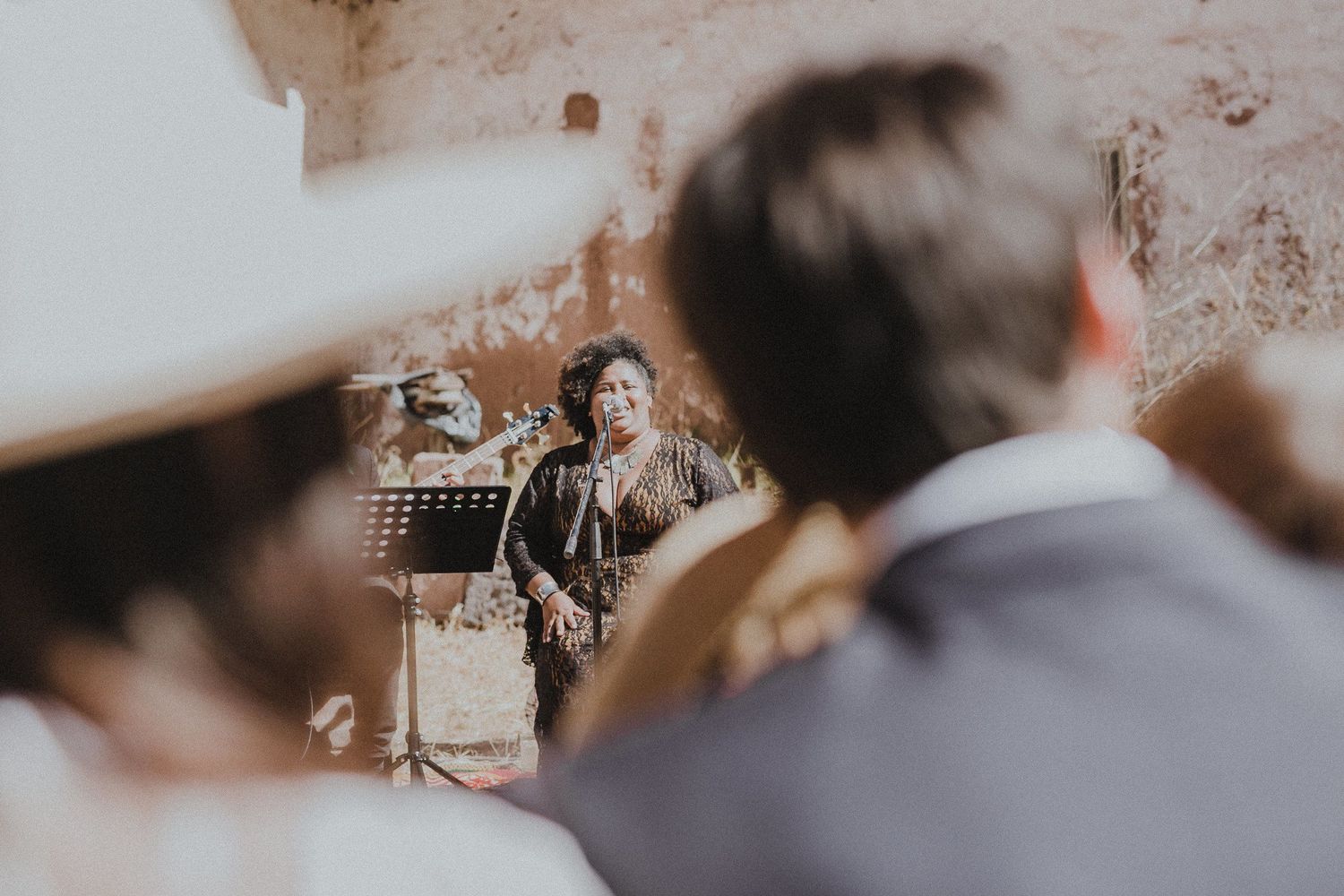 Guests watching a wedding ceremony through foreground shoulders in a rustic setting.