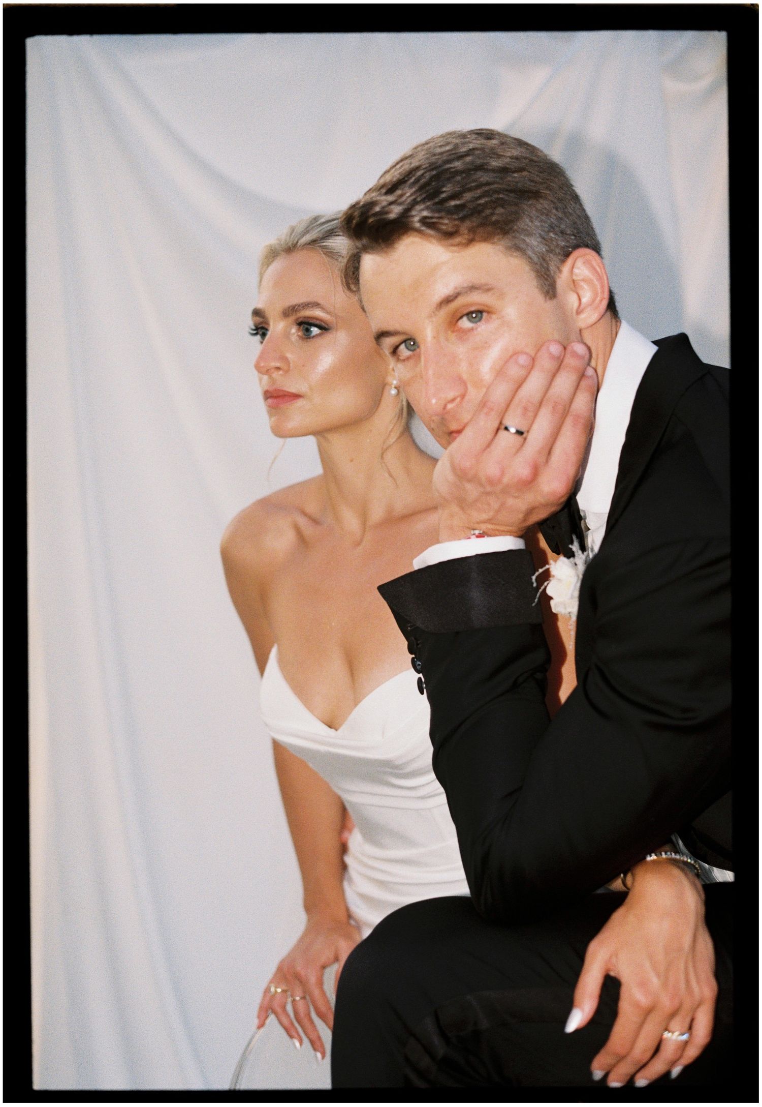 Wedding couple posing together against white backdrop in formal attire.