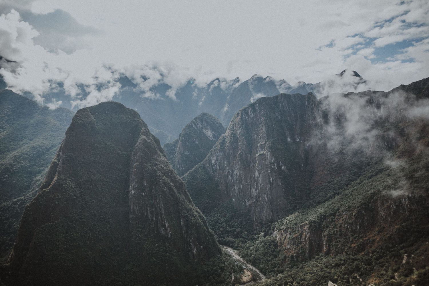 Sweeping vista of jagged mountain peaks and valleys in Machu Picchu with dramatic cloud cover.
