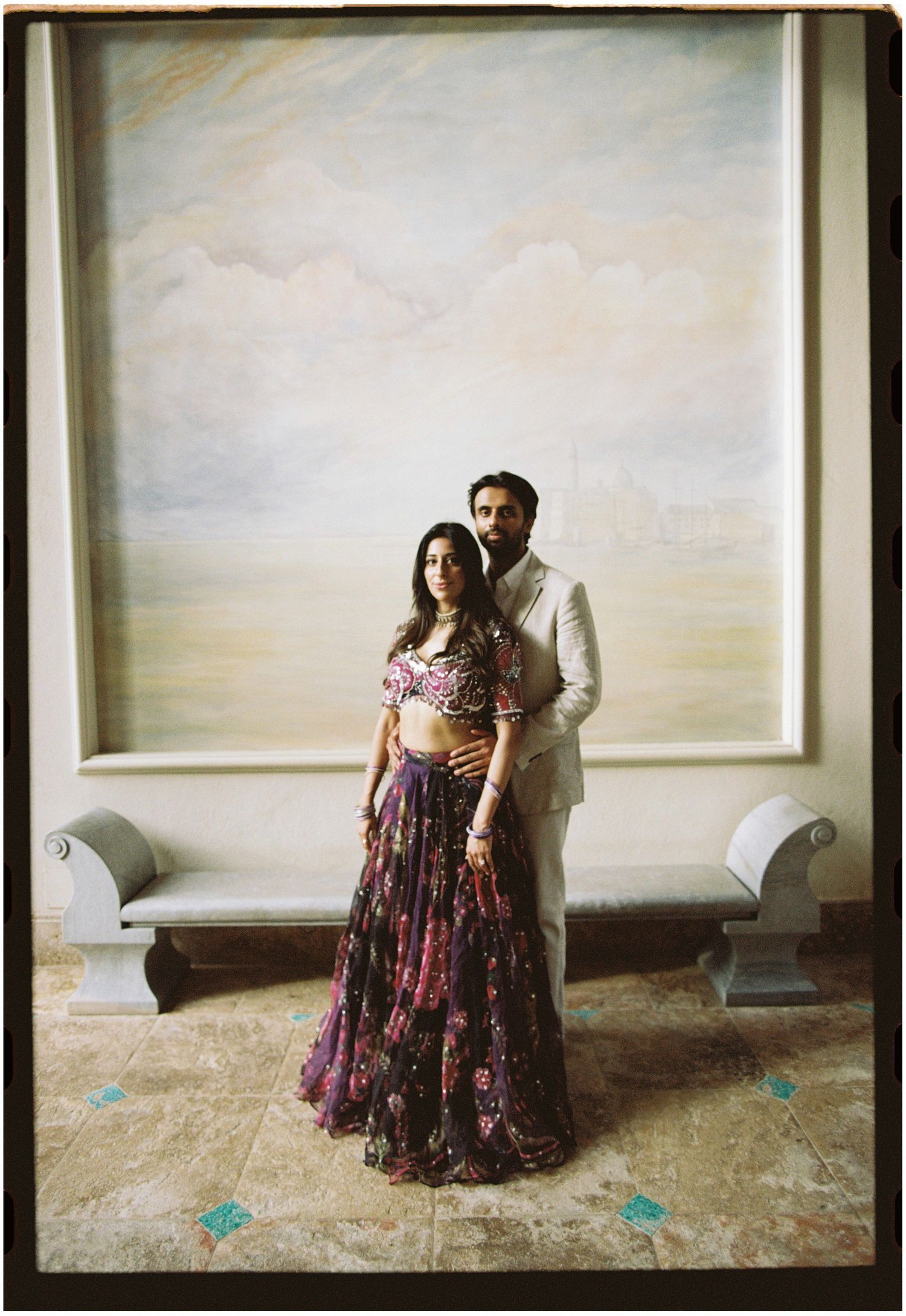 Film portrait of Elina and Jag standing beneath a large painting inside the palace.