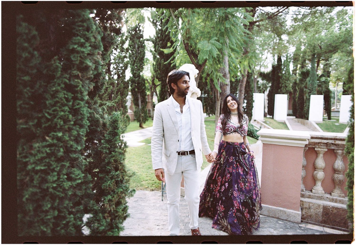 Elina and Jag walking hand in hand through the cypress-lined gardens at Villa Padierna, photographed on film.