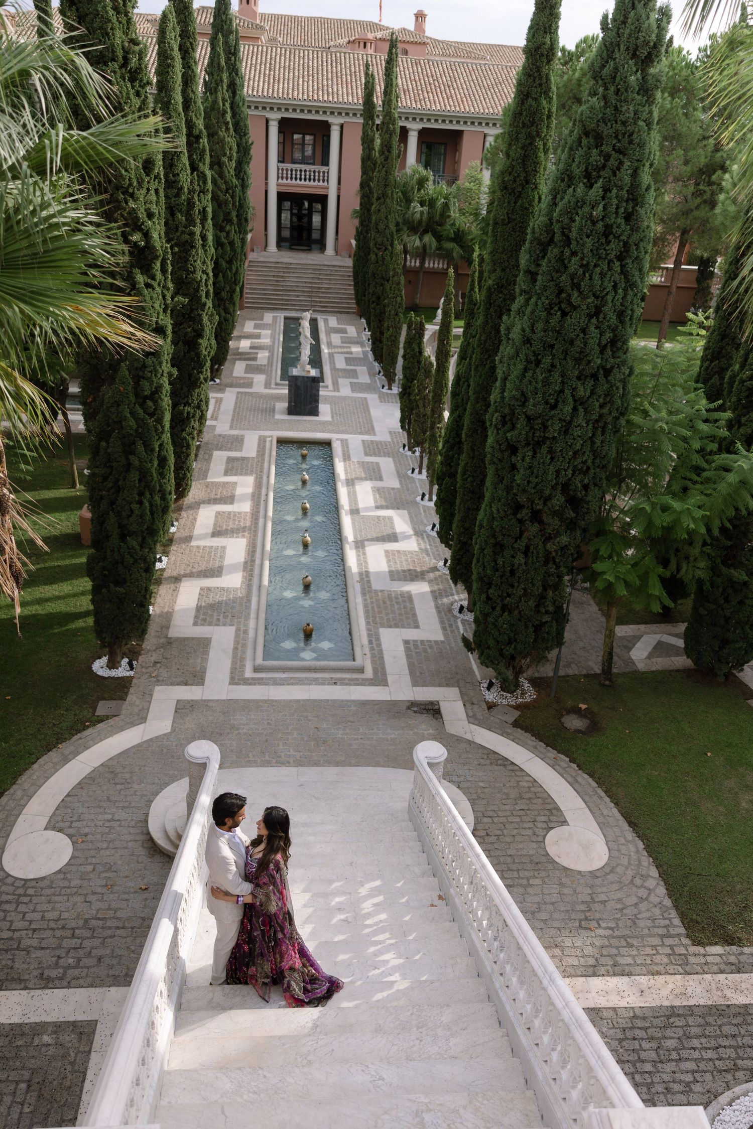 Wide view of Elina and Jag on the staircase above the formal garden and water feature.