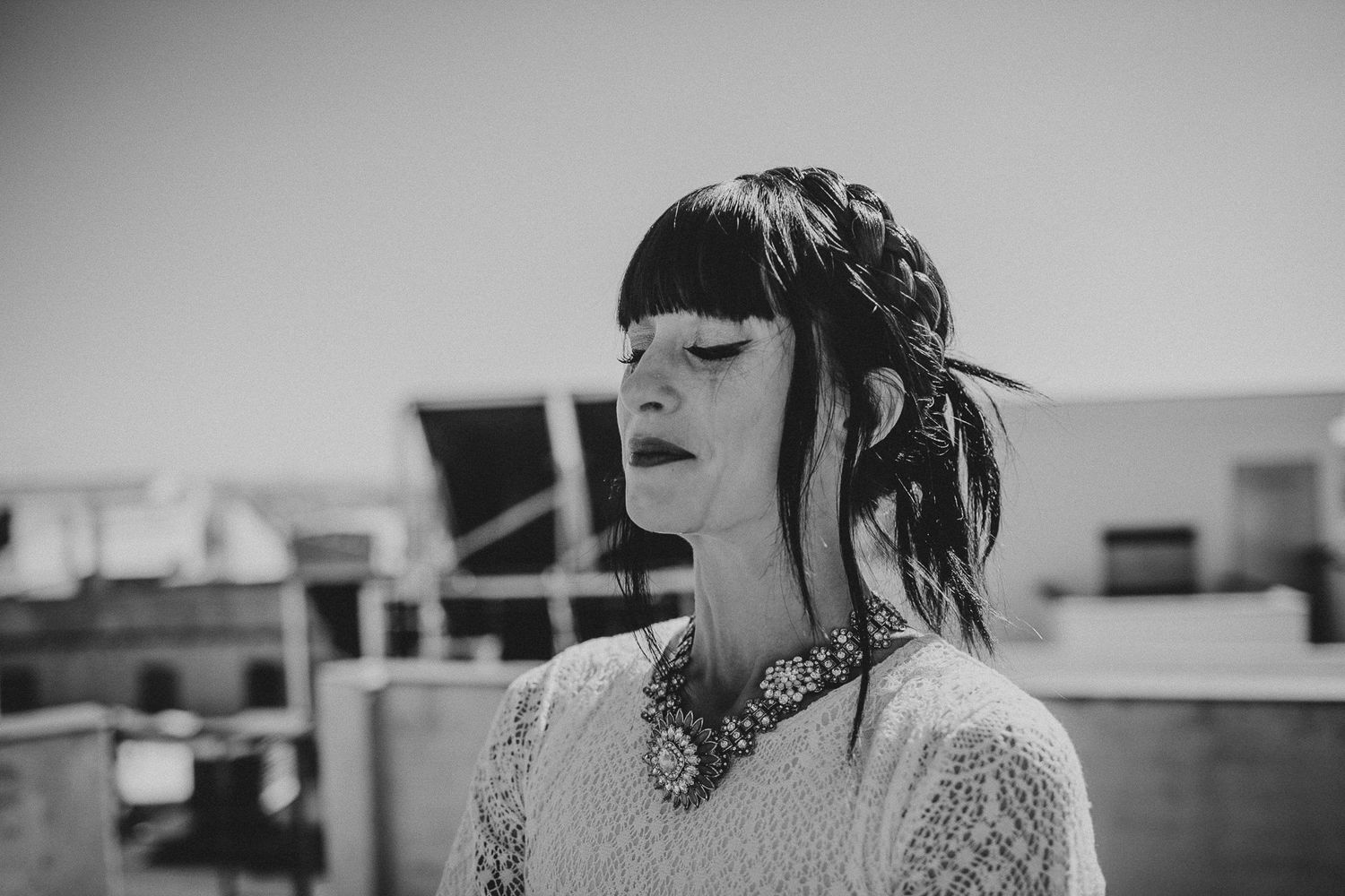 Black and white portrait of a woman wearing a statement necklace and lace dress on an urban rooftop.