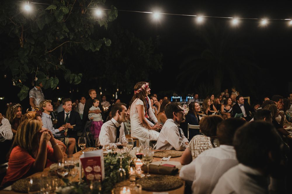 Wedding guests gather under string lights at an outdoor evening reception celebration.