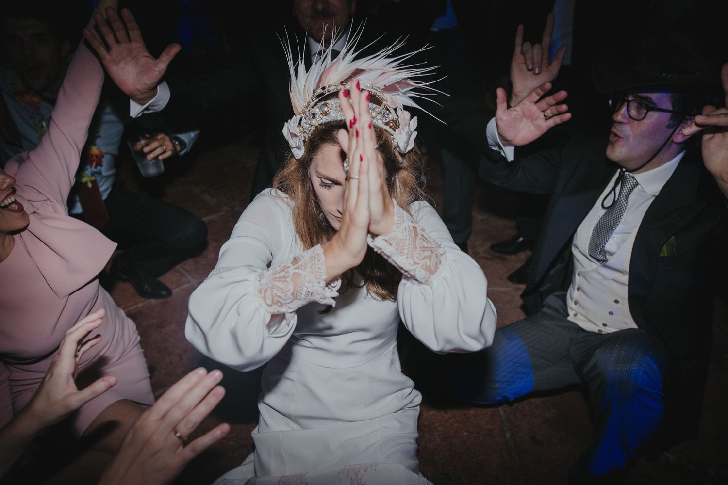Wedding guest in white dress and feathered headpiece dancing among party crowd.