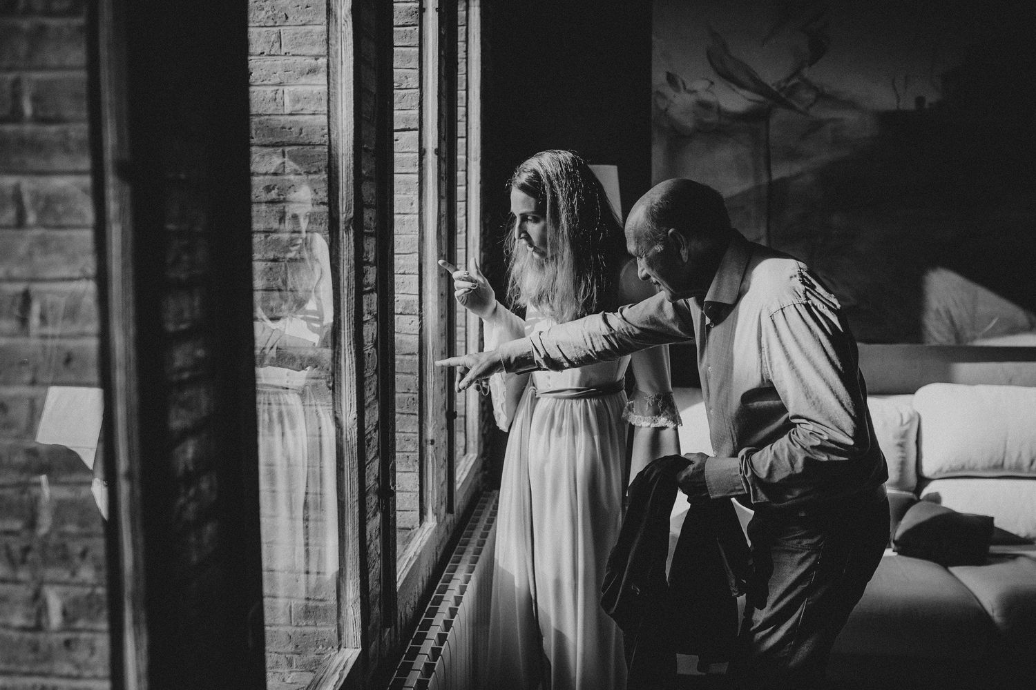 Two figures looking through a large window in an intimate black and white photograph.