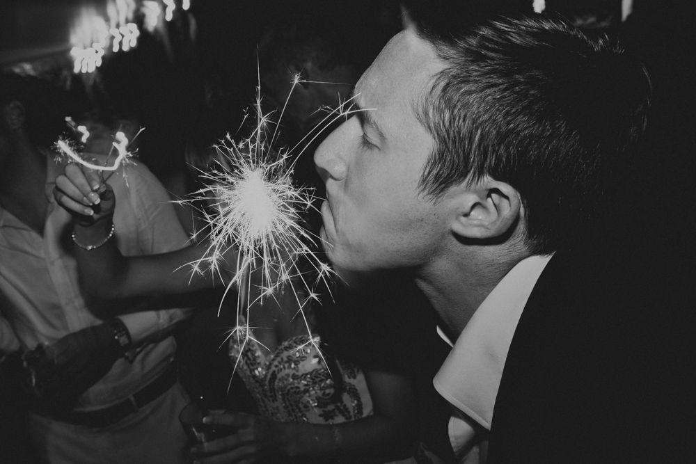Person lighting sparklers during nighttime celebration with drinks.