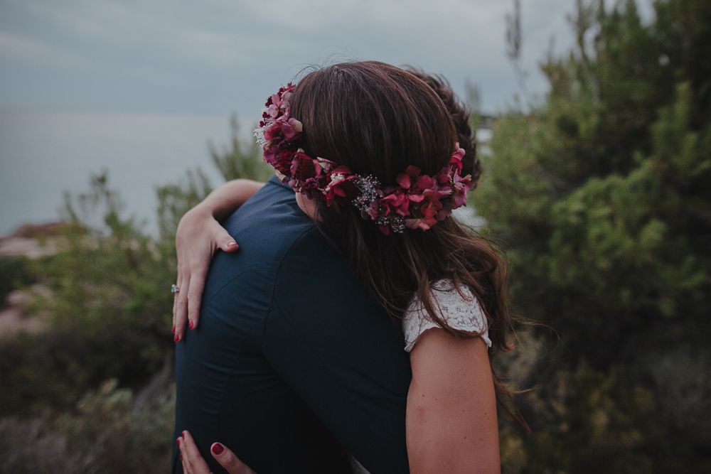 A romantic embrace captured from behind, with the bride wearing a pink floral crown.