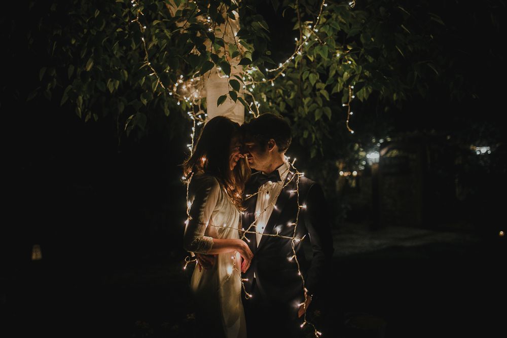 Romantic nighttime scene with string lights illuminating a couple in an intimate embrace.