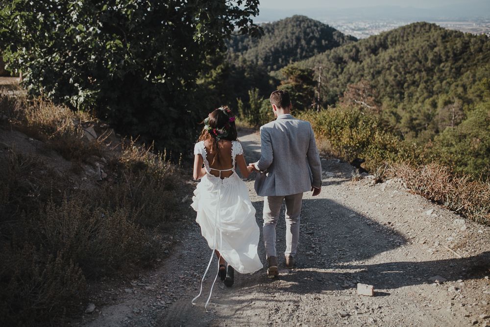 Couple walking hand in hand on mountain path in wedding attire.