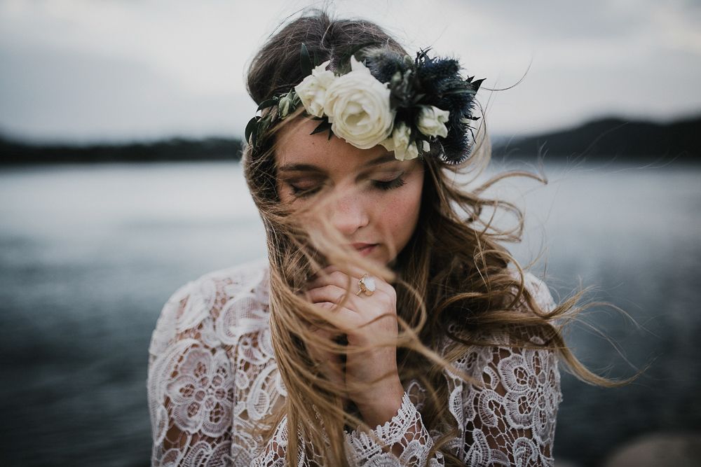 Ethereal portrait of a person wearing a lace dress and floral crown by a misty lake.