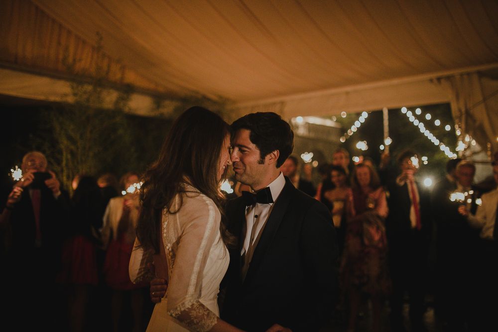 Intimate moment between couple during wedding reception under string lights in tent.
