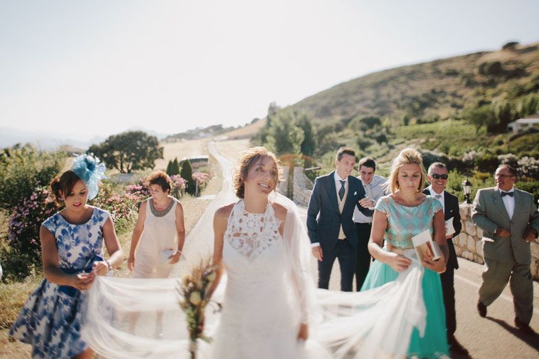 Wedding party walking together on hillside path during sunny outdoor celebration.