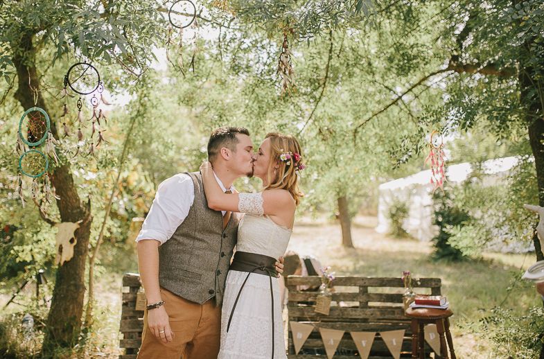 A romantic outdoor wedding moment captured between a couple under trees with vintage decorations and bubbles.