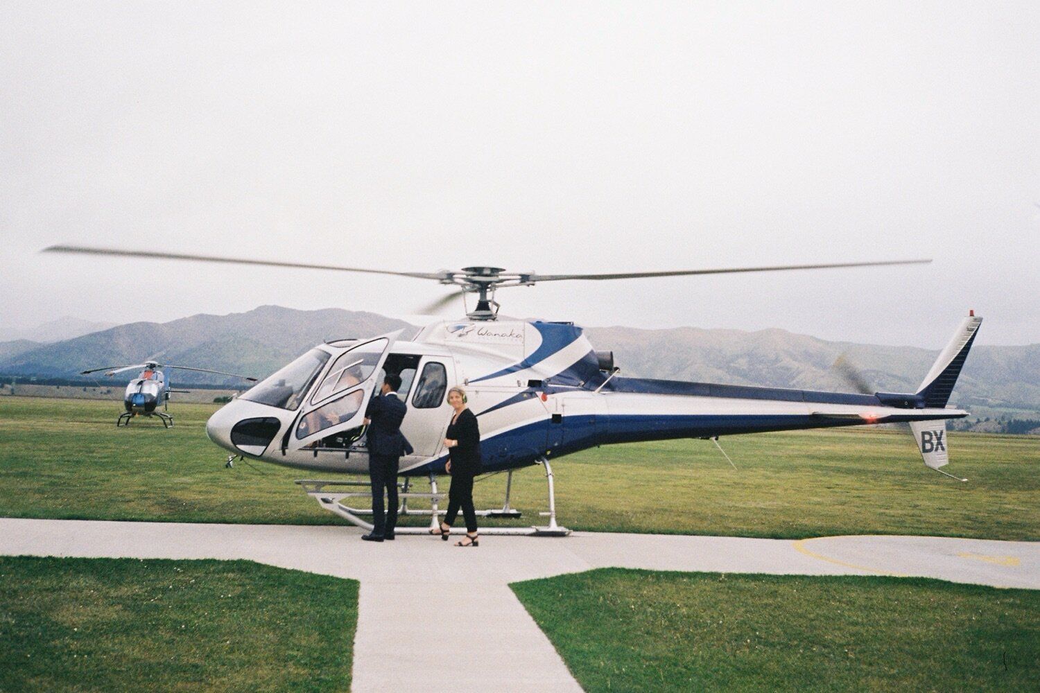 Helicopter wedding transportation with couple standing on helipad.