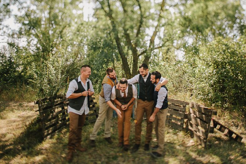 Wedding party in matching vests and pants share a candid moment in outdoor garden setting.