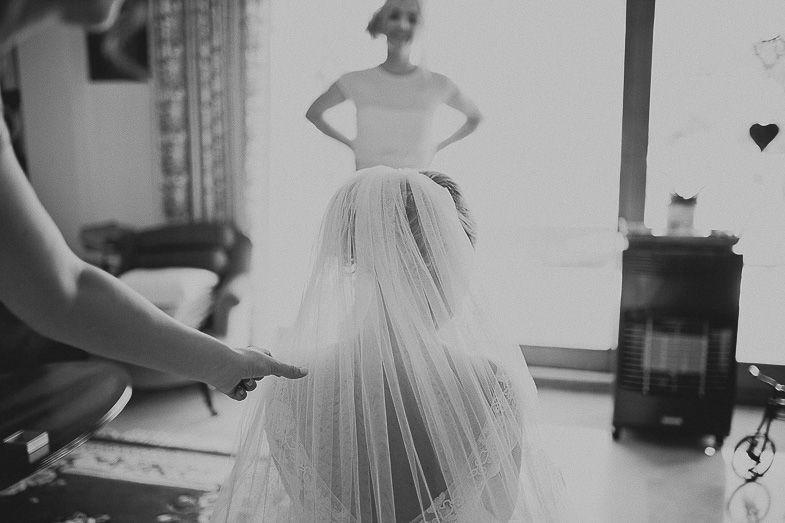 A flowing white wedding dress and veil being adjusted in a black and white photo.