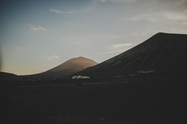 Dark silhouettes of desert mountains at sunset with a small white building in the distance.