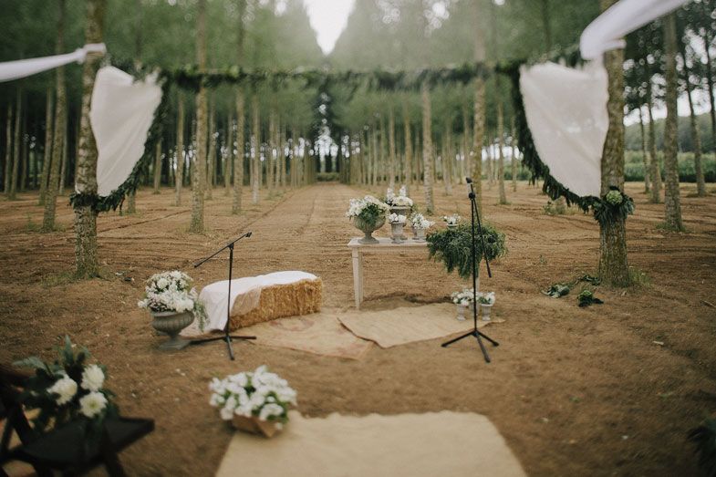 Wedding ceremony aisle decorated with white fabric and flowers in a pine forest.