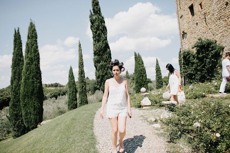 Tall cypress trees line a pathway near an ancient stone building in Tuscany.