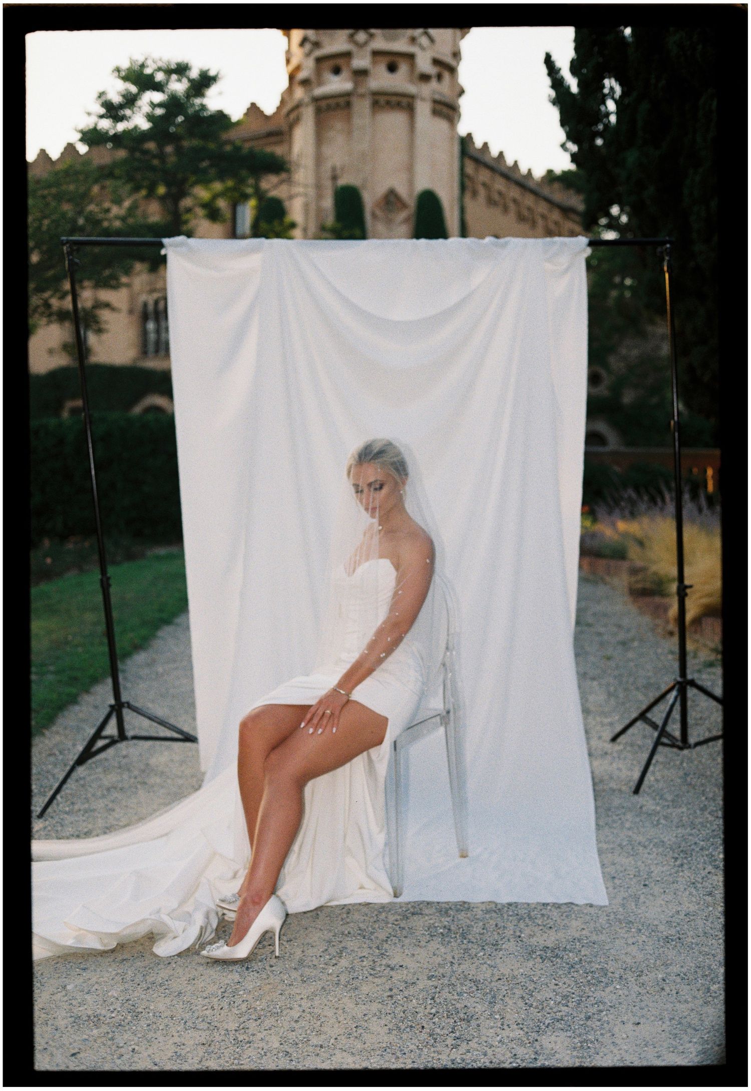 Elegant bridal photoshoot against white backdrop with castle tower visible in background.