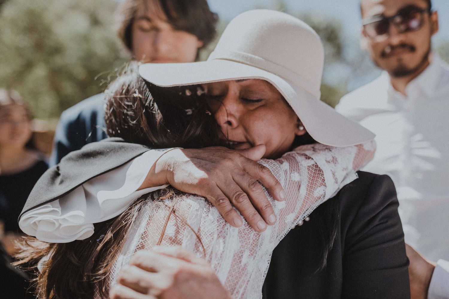 Heartfelt embrace between wedding attendees wearing formal attire at outdoor celebration.