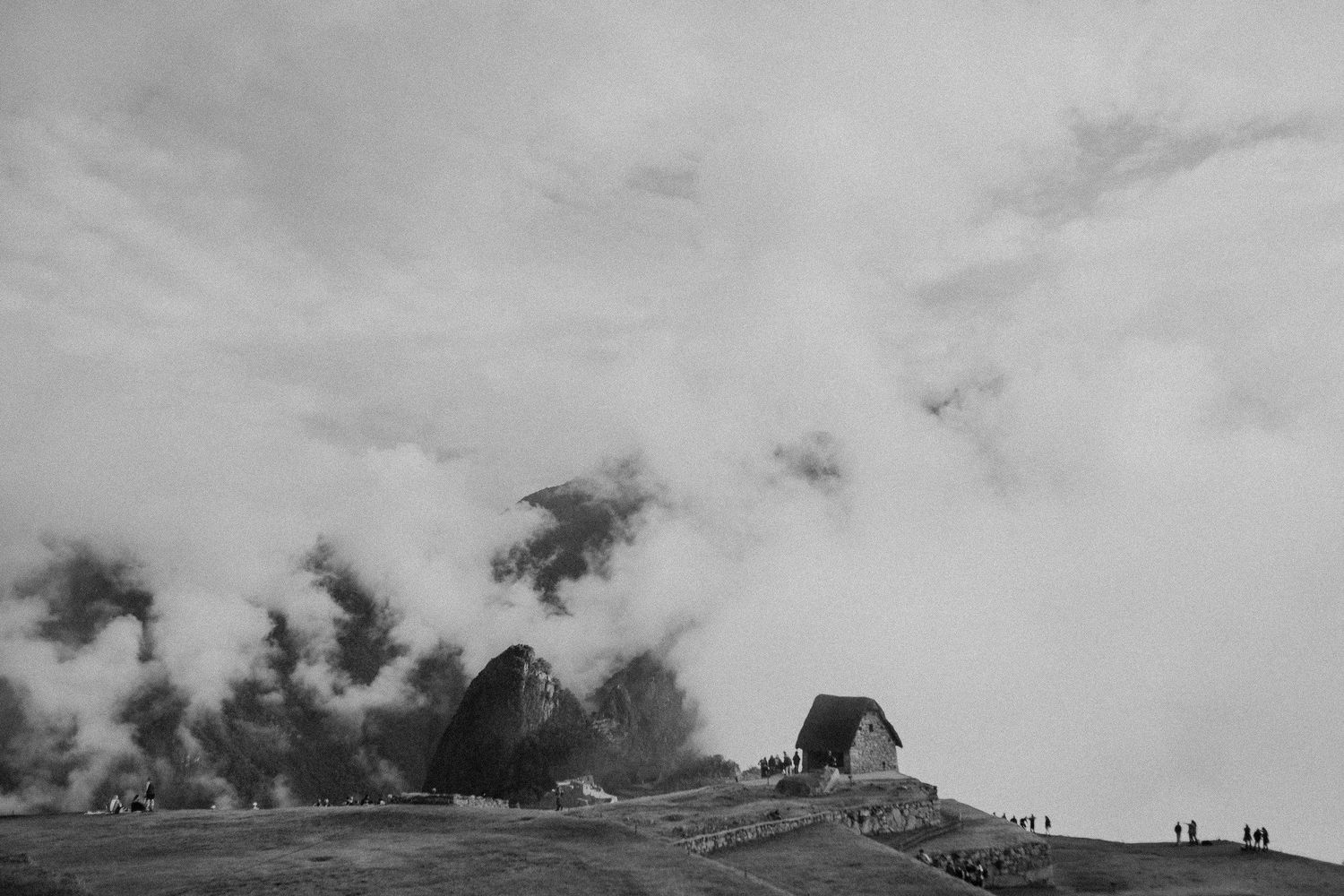 Dramatic black and white landscape with a small house amid rising smoke or clouds.
