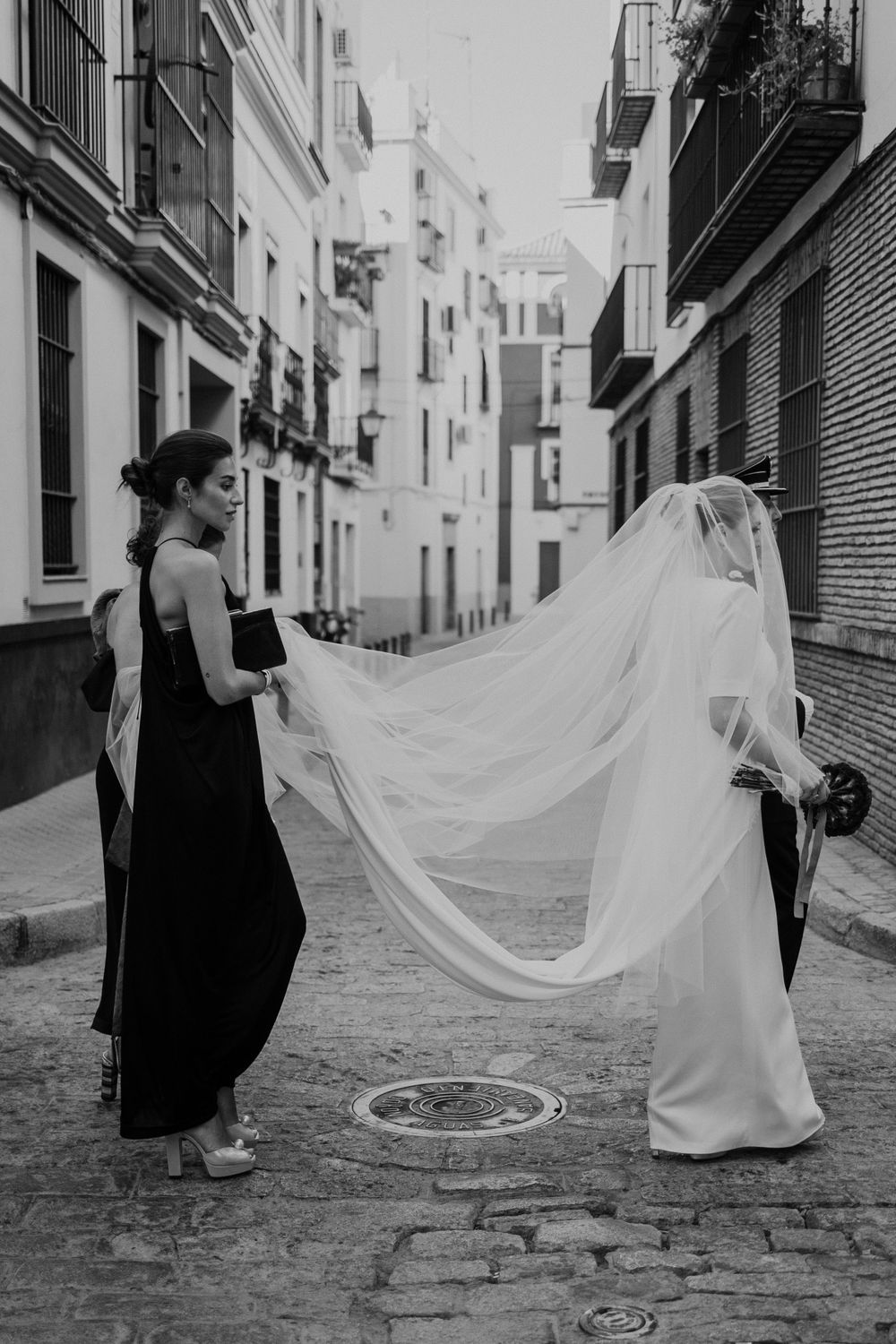 A black and white photo of wedding dress preparation in a narrow European street.