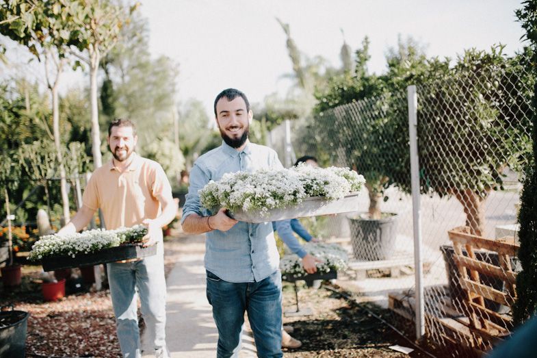Men carrying large garlands of white flowers through a garden setting.
