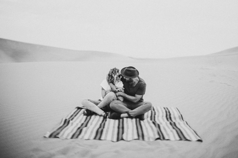 Romantic couple sitting on striped blanket in desert sand dunes.