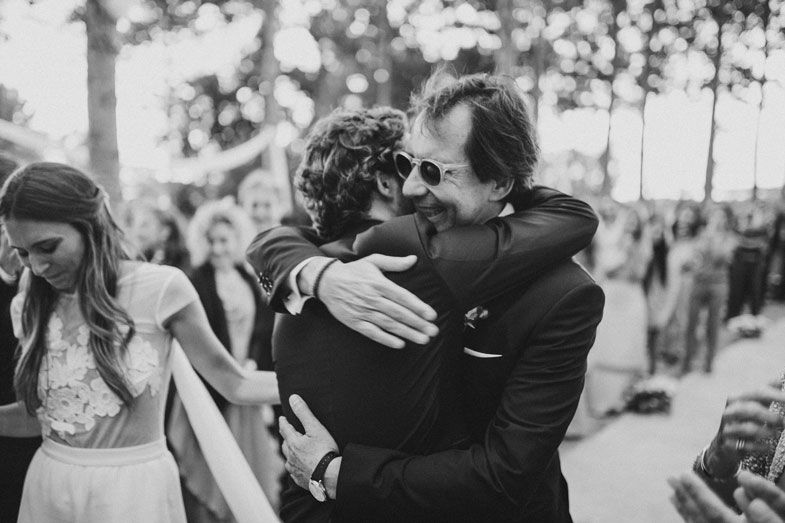 Emotional embrace at outdoor wedding celebration surrounded by trees.
