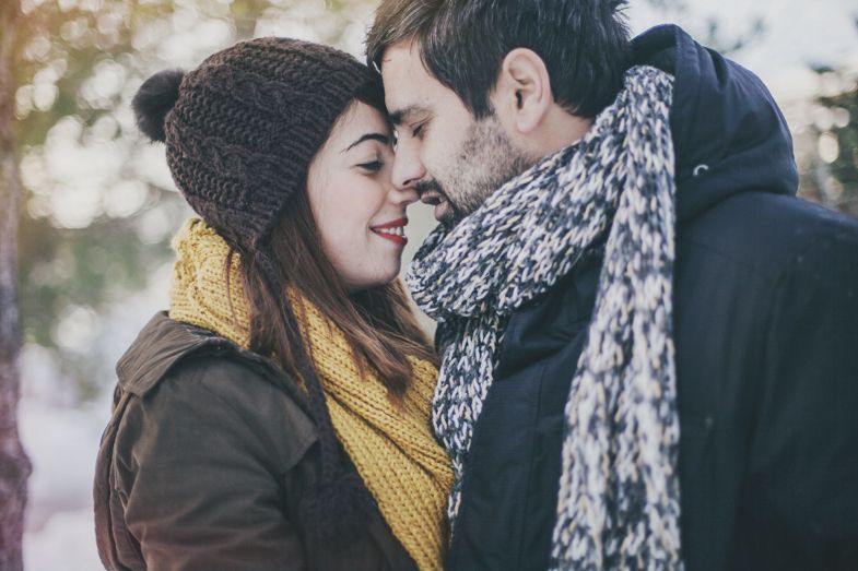 A cozy winter scene with two people in warm scarves and hats sharing an intimate moment outdoors.