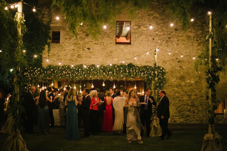 Wedding guests gathered in front of a stone wall decorated with string lights and greenery.